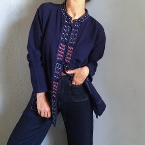 Puede incluir: Chaqueta azul marino con bordados blancos y coral. La chaqueta tiene cuello mandarín y cierre de botones. El bordado está en la parte delantera y alrededor del cuello. La chaqueta se combina con vaqueros de mezclilla azul oscuro.