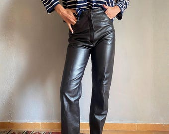 May include: Black leather pants with a straight leg design. The pants have a classic, tailored fit and a smooth, shiny texture. The pants are paired with a navy and white striped long-sleeve shirt.