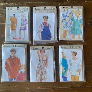 Puede incluir: Seis patrones de costura Burda vintage en fundas de plástico. Los patrones presentan ilustraciones de varios diseños de ropa, incluyendo vestidos, monos y abrigos. Los patrones están etiquetados con el logotipo de Burda y los números de patrón.