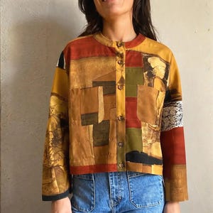 Könnte beinhalten: Eine langärmelige Knopfjacke mit Patchwork-Design in Senfgelb, gebranntem Orange, Olivgrün und Schwarz. Das Kleidungsstück verfügt über zwei Brusttaschen, einen Rundhalsausschnitt und einen grafischen Druck einer menschlichen Figur.