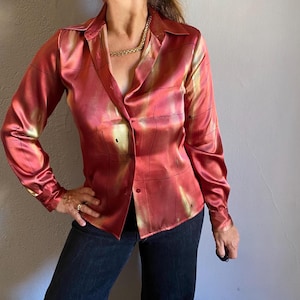 May include: A long-sleeved, button-down shirt in shades of red, yellow, and black. The shirt has a silky, satin-like texture and a subtle geometric pattern. The collar is open, and the shirt is paired with dark blue jeans.