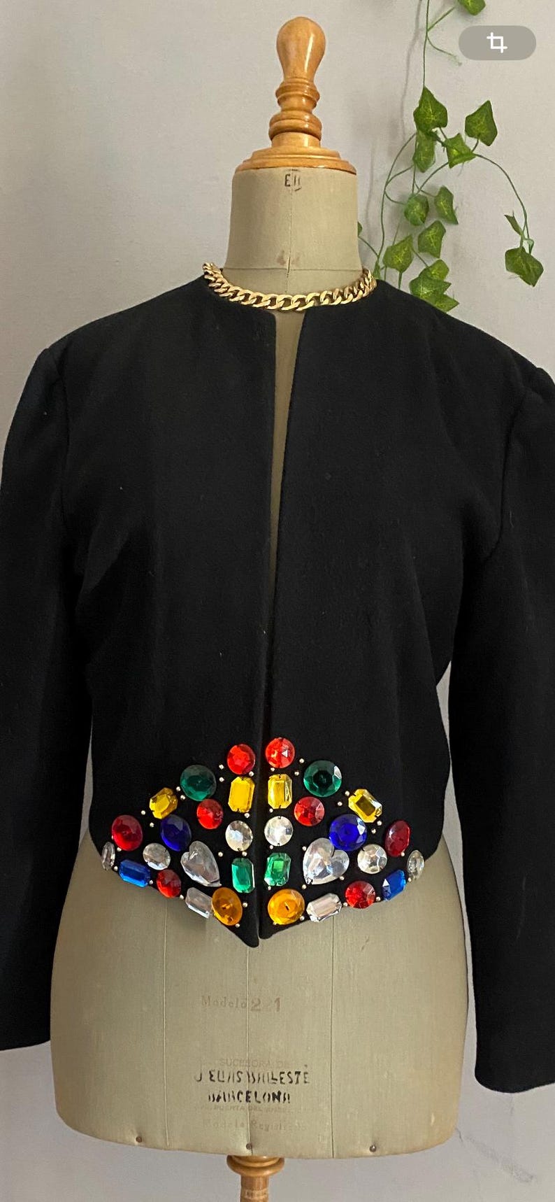 Puede incluir: Chaqueta negra con cuello de cadena dorada y adornos de piedras preciosas de colores. La chaqueta se exhibe en un maniqu&iacute;. El dise&ntilde;o de piedras preciosas presenta una variedad de formas y colores, incluyendo rojo, amarillo, verde y azul.