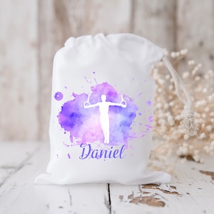May include: White drawstring bag with a purple watercolour design of a person on rings. The bag has the name "Daniel" printed on it.
