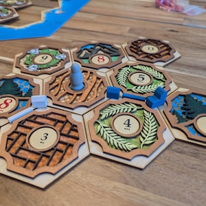 May include: A wooden game board with hexagonal tiles featuring numbers 3, 4, 5, 8, and 9. The tiles are arranged in a circular pattern with a small wooden figure in the center.