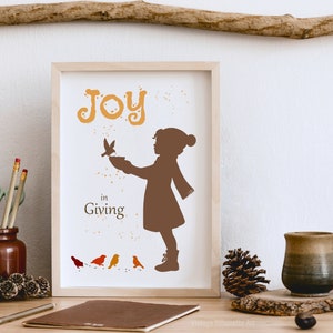 May include: A framed print with a brown silhouette of a child feeding birds. The print has the text "Joy in Giving" and is decorated with orange and yellow paint splatters.