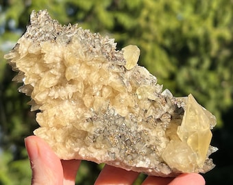 Puede incluir: Un cúmulo de cristales de calcita amarillos con una capa de cristales de pirita en la parte superior. Los cristales de calcita son afilados y puntiagudos, mientras que los cristales de pirita son pequeños y brillantes.
