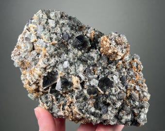 May include: A cluster of green fluorite crystals with black inclusions, set in a matrix of brown and white minerals. The crystals are sharp and well-defined, with a glassy lustre.