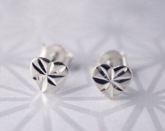 May include: A pair of silver heart-shaped stud earrings with a diamond-like pattern on the front.