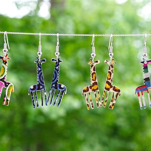 May include: A set of six giraffe-shaped earrings, each with a different patterned design. The earrings are made of metal and have silver hooks. The patterns include colorful geometric shapes, stripes, and animal prints.