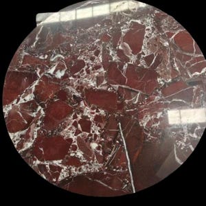 Puede incluir: Encimera circular con un llamativo patrón de mármol rojo. La superficie presenta grandes vetas irregulares de color burdeos y blanco, creando un diseño audaz y único. Ideal para la decoración del hogar.