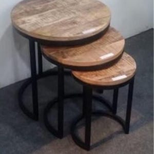 Puede incluir: Tres mesas redondas de madera anidadas con marcos de metal negro. Las mesas están apiladas una encima de la otra, con la mesa más grande en la parte inferior y la mesa más pequeña en la parte superior.