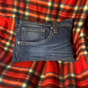 May include: A blue denim pillow with a single pocket on the front, resting on a red and black tartan blanket.