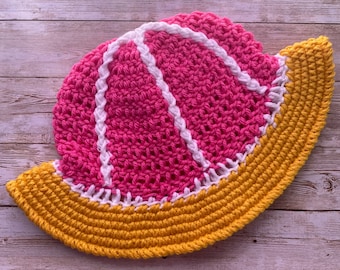 Può includere: Un cappello all'uncinetto fatto a mano in una vivace combinazione di colori. Il cappello presenta una corona rosa brillante con dettagli bianchi e una tesa gialla. Il lavoro all'uncinetto è visibile, mostrando la consistenza e l'artigianalità del pezzo.