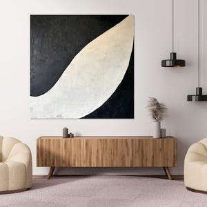 Puede incluir: Una pintura abstracta en blanco y negro con una forma curva en el centro. La pintura está colgada en una pared blanca sobre una consola de madera con dos sillones de color crema.
