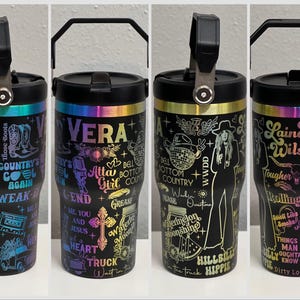 Pode incluir: Quatro copos de a&ccedil;o inoxid&aacute;vel preto com detalhes arco-&iacute;ris coloridos e designs variados. Os copos apresentam diferentes textos e gr&aacute;ficos, incluindo "Vera", "Atta Girl", "Hillbilly Hippie" e "Lainey Wilson".