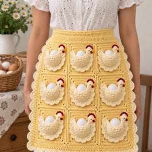 Peut inclure: Un tablier en crochet jaune composé d'une grille de neuf carrés, chacun orné d'un motif de poule en relief de couleur crème. Chaque poche en forme de poule contient un œuf blanc. Le tablier présente une bordure festonnée sur le bas.