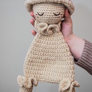 May include: A crocheted mushroom-shaped stuffed toy with a red cap and beige body. The toy has a sweet, smiling face with closed eyes and a ruffled collar.