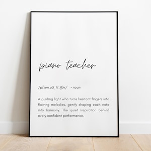 May include: A framed print with the words "piano teacher" in a stylish script font. Below, a definition describes the role of a piano teacher. The print is in a black frame, set against a white wall and wooden floor.
