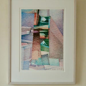 Puede incluir: Impresión artística abstracta en un marco de madera clara. La obra presenta un diseño geométrico colorido con tonos de azul, verde, naranja y marrón. La impresión está firmada en la esquina inferior derecha.