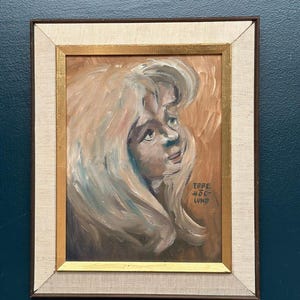 May include: An oil painting on canvas depicting a portrait of a person with long, flowing blonde hair, rendered in expressive brushstrokes with a brown background. The artwork is signed Ebbe Moe Lund and is housed in a gold and beige frame.