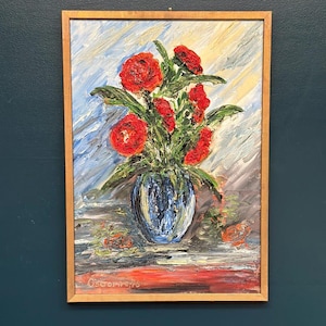 May include: An oil painting in a light wood frame depicting a bouquet of vibrant red flowers in a dark blue vase. The textured brushstrokes create a dynamic background of blue, white, and grey tones. The artist's signature is visible in the bottom left.