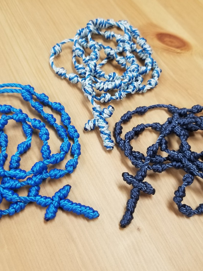 K&ouml;nnte beinhalten: Drei gekn&uuml;pfte Rosenkr&auml;nze aus Seil mit Holzperlen und Kreuzen. Ein Rosenkranz ist blau, einer ist wei&szlig; und blau und einer ist dunkelblau.