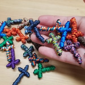 May include: A collection of colourful, knotted, cross-shaped charms. The charms are made of various colours of thread, including blue, green, red, orange, purple, and brown.