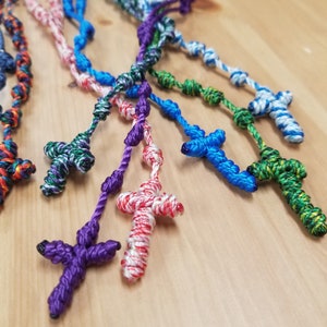 K&ouml;nnte beinhalten: Eine Sammlung bunter, gekn&uuml;pfter Rosenkr&auml;nze aus Seil mit verschiedenen farbigen Kreuzen. Die Rosenkr&auml;nze bestehen aus verschiedenen Farben von Schnur, darunter Lila, Blau, Gr&uuml;n, Rot und Wei&szlig;.