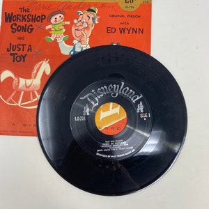 K&ouml;nnte beinhalten: Eine schwarze Schallplatte mit einem roten und gelben Etikett, auf dem "Disneyland" und "Seite 1" steht. Die Schallplatte ist aus Walt Disneys "Babes in Toyland" und enth&auml;lt den Song "The Workshop Song" mit Ed Wynn. Die Schallplatte ist 45 U/min und stammt von Walt Disney Productions.