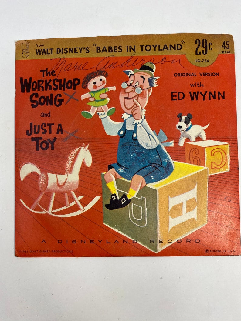 K&ouml;nnte beinhalten: Ein rotes und wei&szlig;es Schallplattencover mit einer Cartoon-Illustration eines Mannes, der eine Puppe, ein Schaukelpferd und einen Hund h&auml;lt. Die Schallplatte tr&auml;gt den Titel "The Workshop Song and Just a Toy" und den Text "from Walt Disney's "Babes in Toyland" 29c 45 RPM LG-724 Original Version with Ed Wynn".