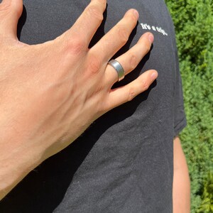 May include: A silver band ring on a person's finger. The ring is a simple, flat band with a smooth surface.