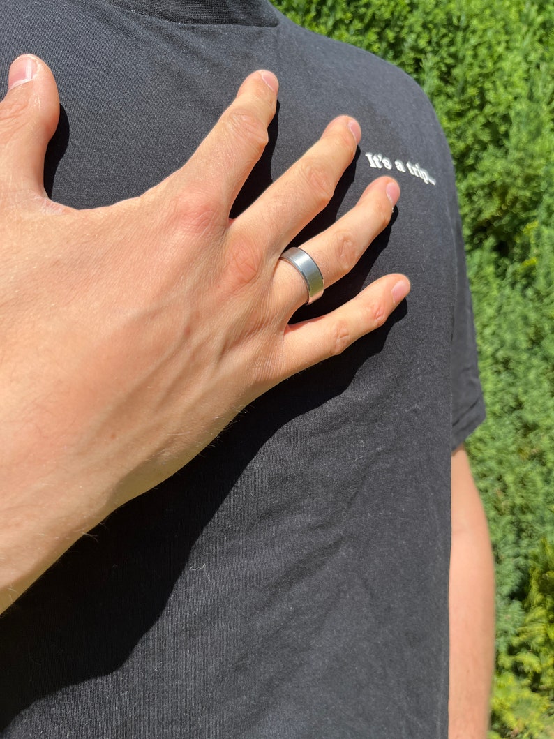 May include: A silver band ring on a person's finger. The ring is a simple, flat band with a smooth surface.