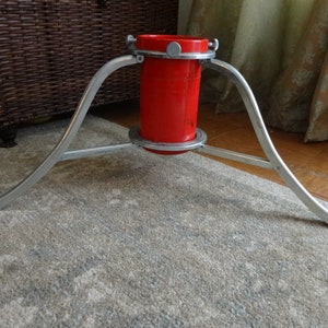 May include: A silver metal Christmas tree stand with three legs and a red plastic water reservoir.