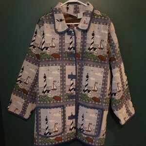 May include: A long-sleeved button-down jacket featuring a repeating grid pattern of lighthouses and sailboats. The fabric is light blue, white, and brown, with a structured collar and blue trim along the edges, pockets, and front button closure.