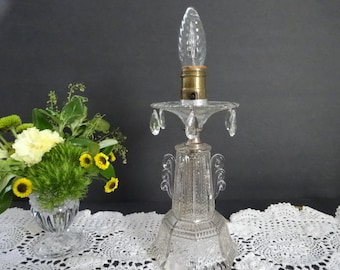 May include: A clear glass lamp with a crystal-like design and a teardrop-shaped bulb. The lamp has a base with a decorative pattern and is adorned with crystal-like accents.
