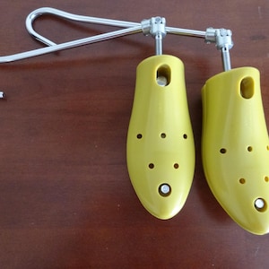 May include: A pair of yellow shoe trees with a silver metal frame and hook. The shoe trees have multiple ventilation holes and are designed to maintain the shape of shoes. The hook allows for easy storage.