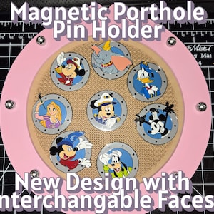 May include: A pink magnetic pin holder with interchangeable faces, featuring Disney characters like Mickey Mouse, Donald Duck, and Dumbo. The holder has a circular design with a light brown center and silver accents. Text on the image reads "Magnetic Porthole Pin Holder" and "New Design with Interchangeable Faces."