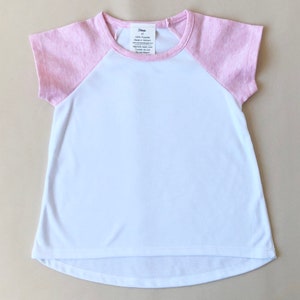 May include: A white and pink baseball tee shirt with short sleeves. The shirt has a pink trim around the neck and sleeves. The shirt has a tag on the front that says "Threads" and has care instructions.