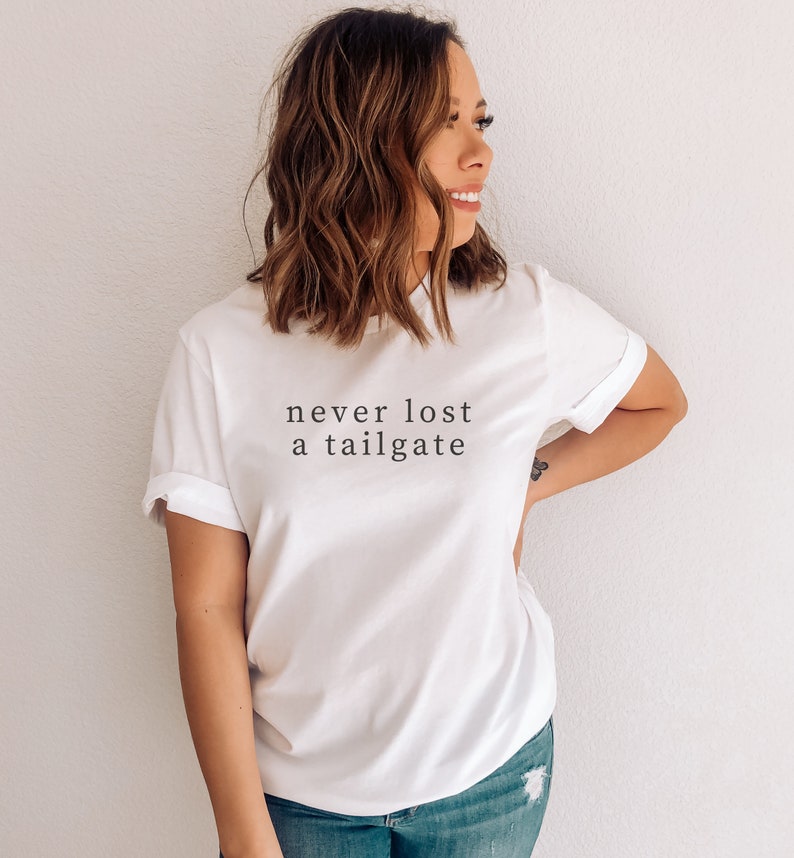 May include: White t-shirt with rolled-up sleeves featuring the text "never lost a tailgate" in a simple, black font. The shirt is made of a soft material and is suitable for casual wear.