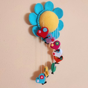 May include: A crocheted baby mobile with a blue flower and colourful butterflies hanging from it. The mobile is made of yarn and has a yellow centre.