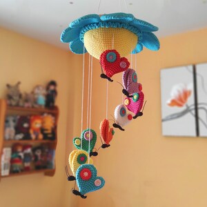 May include: A colourful crocheted baby mobile with a flower-shaped top and hanging butterflies. The butterflies are made of different colours of yarn and have a heart shape.