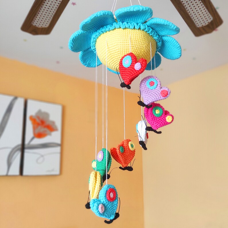 May include: A colourful crocheted baby mobile with a yellow sun and butterflies in various colours, including red, pink, orange, green, and blue.