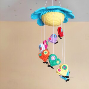 May include: A crocheted baby mobile with a blue and yellow sun and colourful butterflies hanging from it.