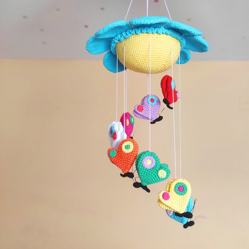 May include: A crocheted baby mobile with a blue and yellow sun and colourful butterflies hanging from it.