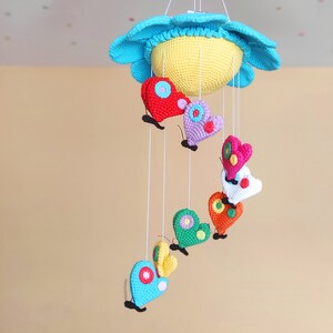 May include: A colourful crocheted baby mobile with a blue and yellow sun and hanging butterflies in various colours, including red, pink, green and purple.