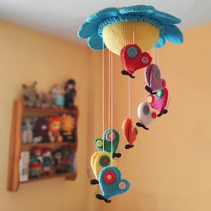 May include: A colourful crocheted baby mobile with a flower-shaped top and hanging butterflies in shades of pink, red, yellow, blue, and green.
