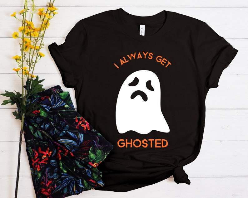 May include: Black t-shirt with the text "I ALWAYS GET GHOSTED" in orange, and a white ghost graphic. The shirt is a casual style, suitable for Halloween or everyday wear.