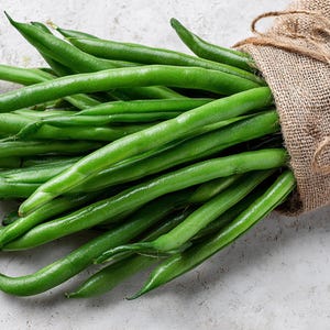 May include: A collection of bright green beans spilling from a hessian sack. The beans are long and slender, with a glossy appearance. The sack is tied with twine, giving a natural, rustic feel. The image showcases fresh produce.