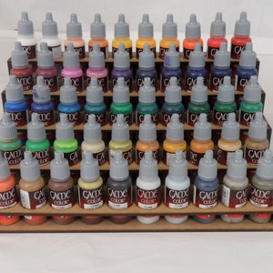 May include: A wooden paint rack with five shelves, each holding rows of small bottles of acrylic paint. The bottles are labelled "Game Color" and have a variety of colours, including red, blue, green, yellow, and brown.