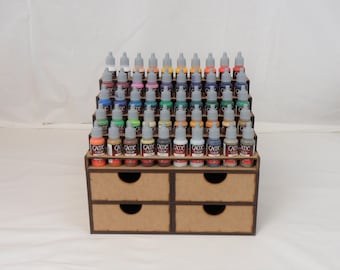 May include: A wooden paint storage rack with four drawers and five shelves, holding rows of small bottles of acrylic paint. The bottles are labeled "CADICE COLOR" and have gray caps.